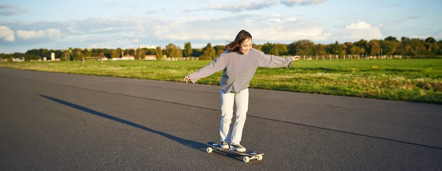 Hobbies and lifestyle. Young woman riding skateboard. Skater girl enjoying cruise on longboard on sunny day outdoors.