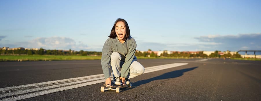 Portrait of carefree, happy asian girl skating, riding skateboard and laughing, enjoying sunny day.