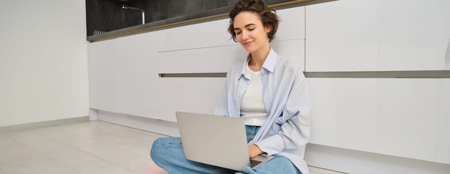 Young woman studying on floor. Girl with laptop works from home, types on computer, smiles and feels creative.