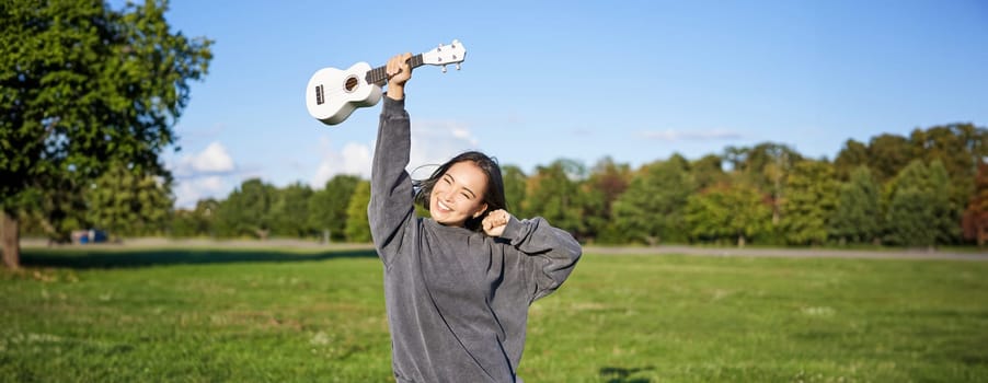 Positive beauty girl with ukulele, dancing and feeling freedom, looking excited, triumphing and celebrating.