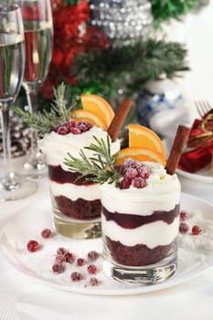 Christmas cranberry dessert tiramisu with mascarpone and whipped cream, chocolate biscuit crumble and cranberry jam, garnished with orange slices, candied cranberries and rosemary.