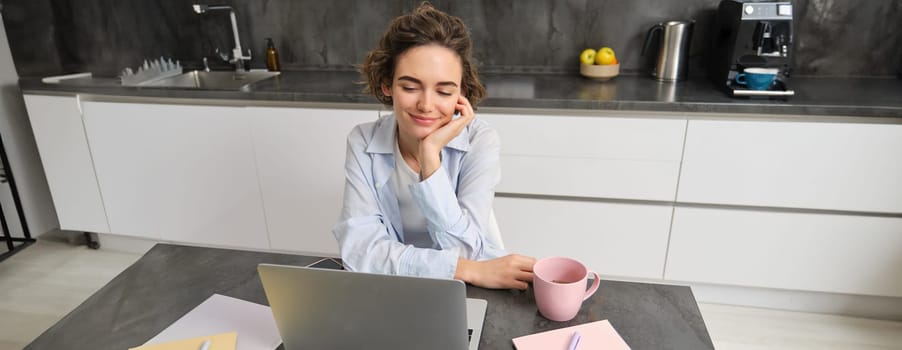 Portrait of young woman looking at computer screen, sitting at home and working, concept of remote education, online webinars and workplace.