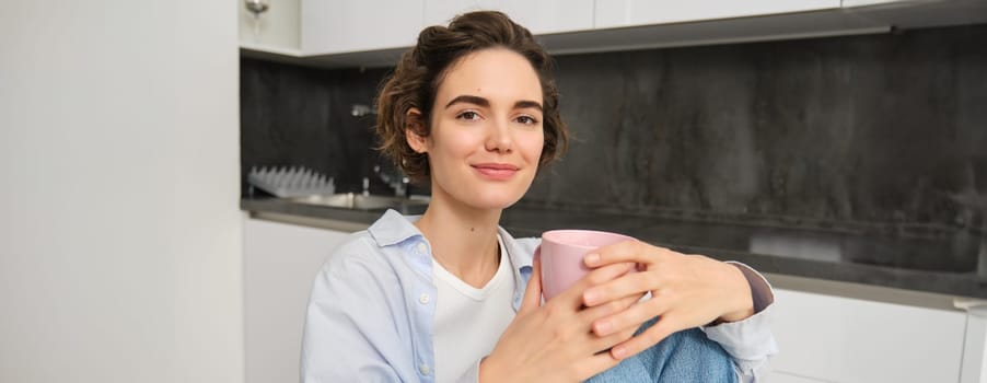 Portrait of smiling woman with cup of tea, drinking hot beverage at home, looking relaxed, enjoying comforting weekend.