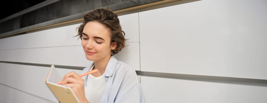 Creative young woman, writes makes notes, sits on floor at home, puts her thoughts on paper, does homework. People, lifestyle and hobbies concept