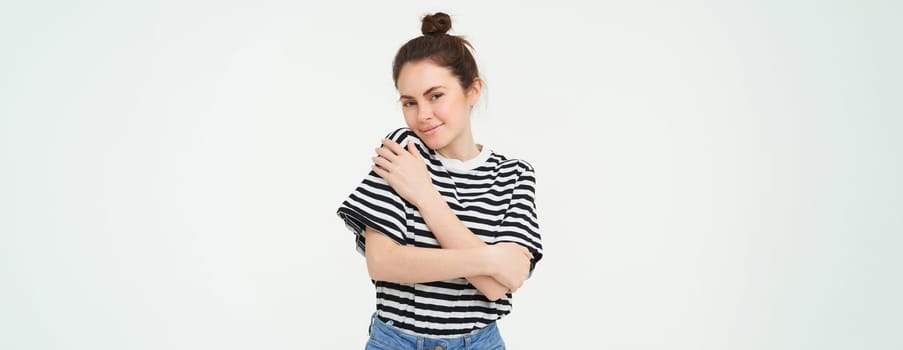 Image of tender, beautiful brunette girl, hugging herself, concept of selfcare and love, standing over white background.