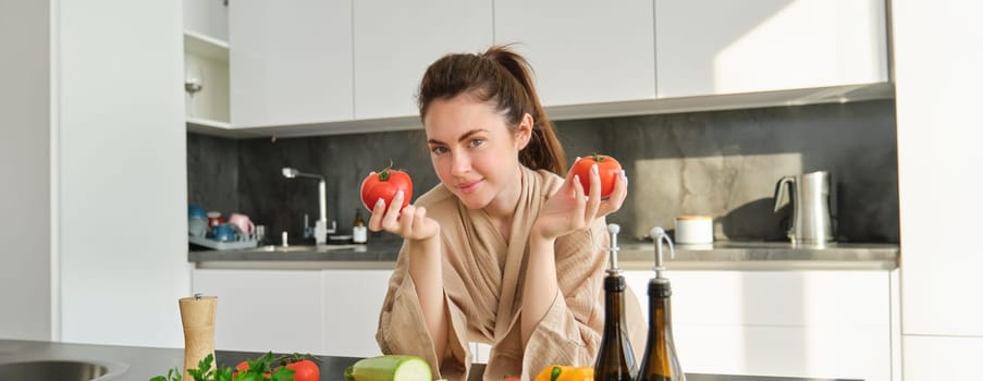 Portrait of woman cooking at home in the kitchen, holding tomatoes, preparing delicious fresh meal with vegetables, standing near chopping board.