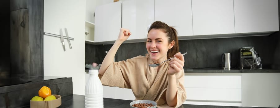 Portrait of happy, laughing young woman eating cereals with milk, triumphing, having breakfast and feeling excited, energetic morning concept.