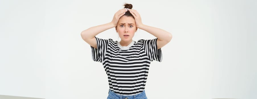 Portrait of woman in trouble, holding hands on head and panicking, looking worried, isolated over white background.