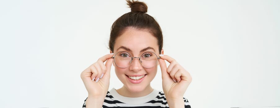 Close up portrait of beautiful woman, trying on new glasses, buying eyewear, smiling and looking happy, standing over white background.