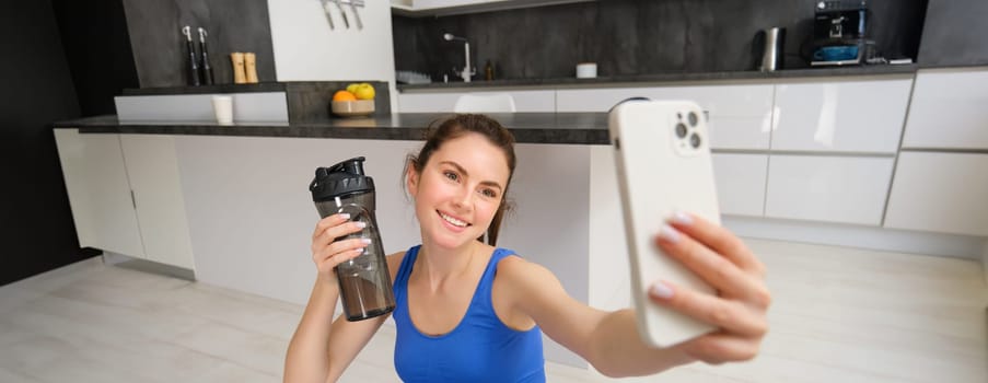 Wellbeing and sports. Beautiful young woman taking selfie on smartphone, doing fitness training from home, drink water, stays hydrated and doing exercises.
