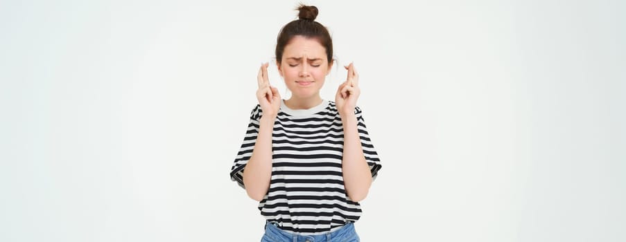 Nervous girl, student cross fingers for good luck, making wish, hoping for something, anticipating positive results, standing over white background.