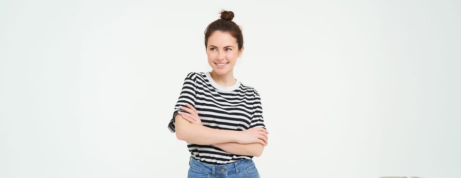 Image of young confident woman in casual outfit, looking happy, standing against white background.