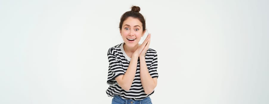 Portrait of amazed young woman, claps hands and gazing at something beautiful, isolated over white background. Copy space