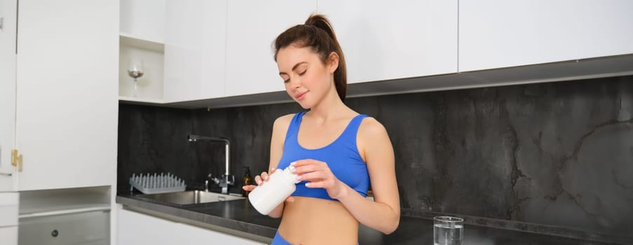 Sport and healthcare. Young woman holding tablets, vitamin c, taking dietary supplements and smiling, leading active and healthy lifestyle, wearing sportswear.