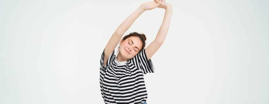 Image of beautiful girl stretching her arms with pleased, satisfied face expression, isolated against white background.