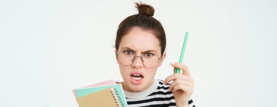 Close up portrait of woman shouting, wearing glasses, shaking pen and holding paperwork, notebooks, teacher arguing, scolding someone, standing over white background.