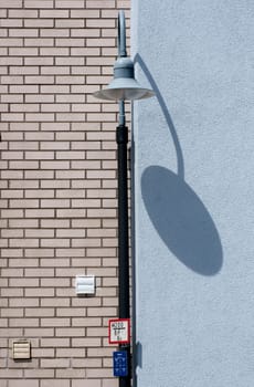 The photograph of a clinkered and plastered facade with the shadow of a lantern.