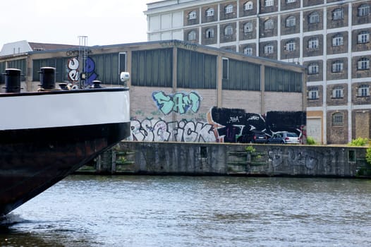 A photograph of a ship's tail passing a warehouse painted with graffiti.