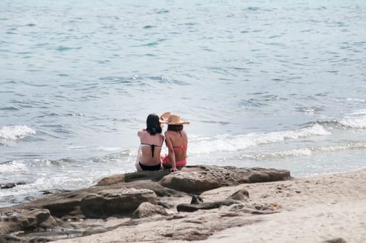 Two girls sitting back on sea beach rock