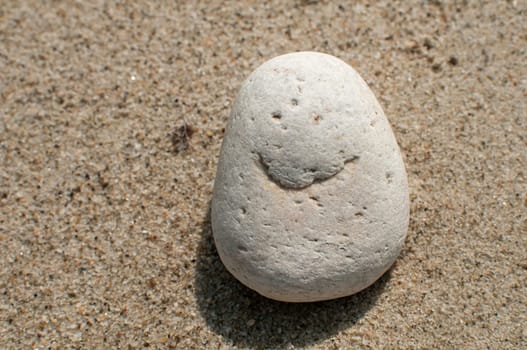 Naturally received image of smile on sea pebble stone on sand background