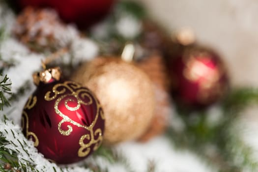 red Christmas baubles between cones and fir branches covered with snow as macro detail