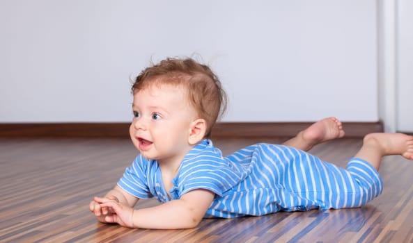 Portrait of a happy 6 months old baby boy crawling on wooden floor at home.