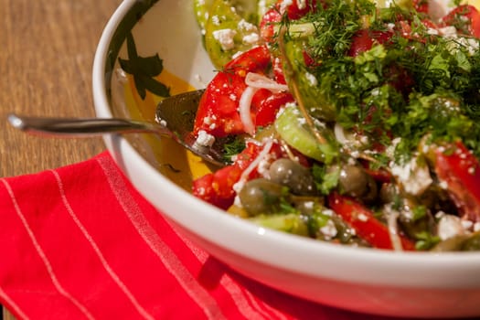 Bowl of marinated Greek salad with tomato cheese and olives on a wood edible