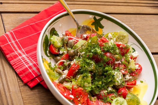 Bowl of marinated Greek salad with tomato cheese and olives on a wood edible