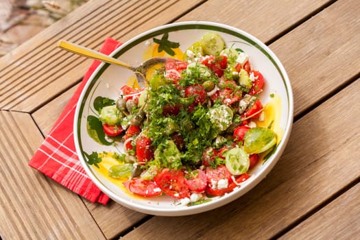 Bowl of marinated Greek salad with tomato cheese and olives on a wood edible