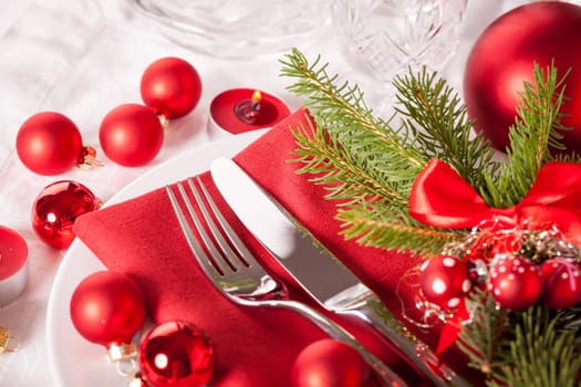 Red napkin with Christmas glass balls and cutlery with a green fir branch and red bow close-up