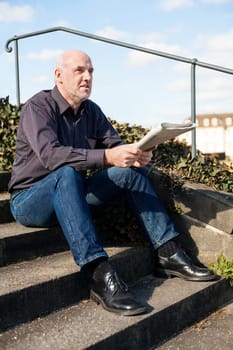 Middle-aged man,senior sitting with a newspaper on a staircase in spring outdoors