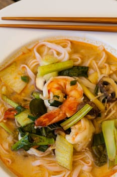 Bowl plate with freshly prepared Tom Yam soup with clanguste and coriander with chopsticks as close-up