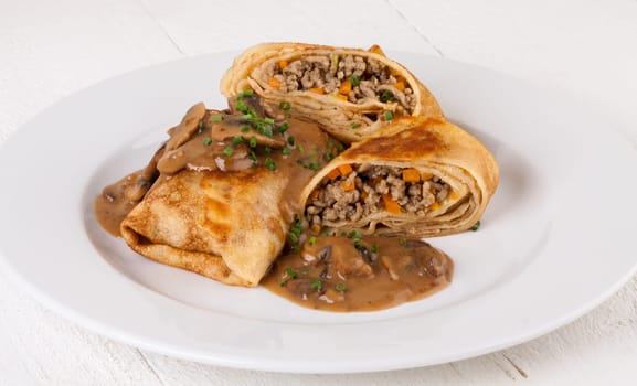 Pancake crepes tortillas stuffed with mushrooms and minced meat on a white plate close-up