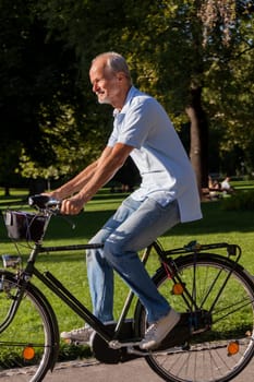 Older man senior pensioner cycling in the park in summer in the sunshine