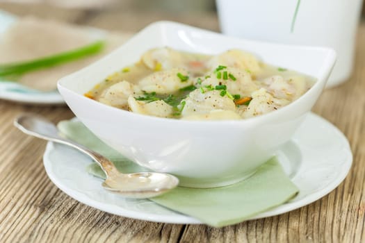 Bowl with Russian Pelmeni Italian tortellini with broth and parsley close-up on a wooden table