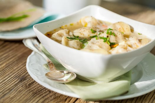 Bowl with Russian Pelmeni Italian tortellini with broth and parsley close-up on a wooden table