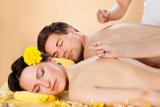 Relaxed young couple receiving acupuncture treatment at beauty spa