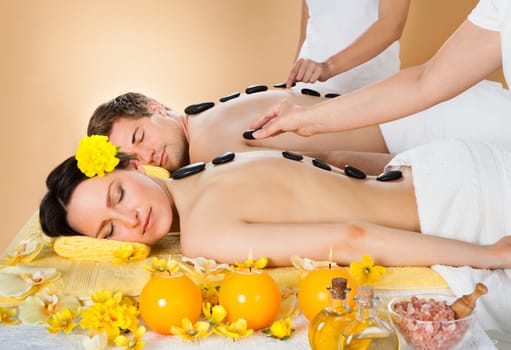 Relaxed young couple receiving hot stone therapy at beauty spa