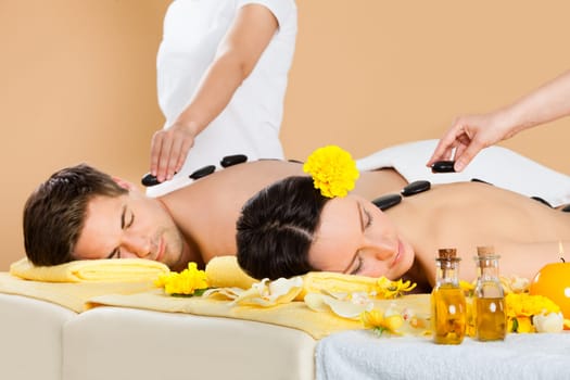Relaxed young couple receiving hot stone therapy at beauty spa