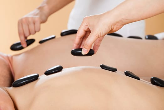 Closeup of young couple receiving hot stone therapy at beauty spa