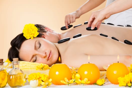 Relaxed young couple receiving hot stone therapy at beauty spa
