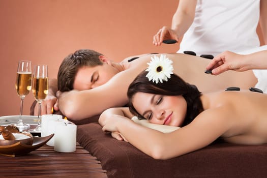 Relaxed young couple receiving hot stone therapy at beauty spa