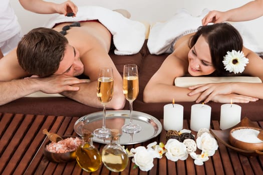 Smiling young couple enjoying hot stone massage at beauty spa