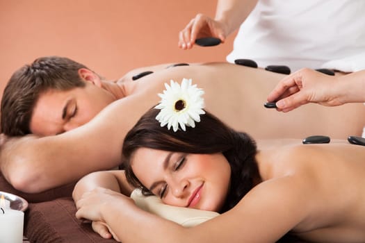 Relaxed young couple receiving hot stone therapy at beauty spa