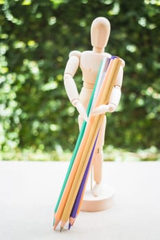 Wooden manikin carrying colour pencil on artist work table, stock photo