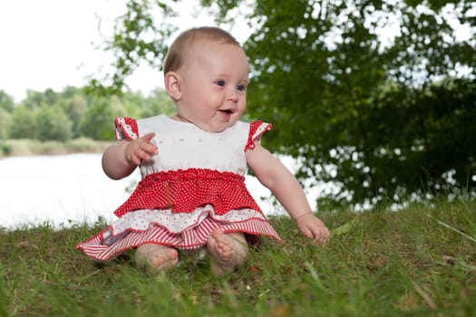 Little baby girl is sitting and playing near the lake