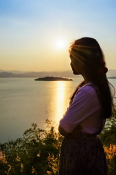 Happy young woman standing on the hill watching the sunset over the lake in Kaeng Kra Chan National Park, Phetchaburi Province, Thailand