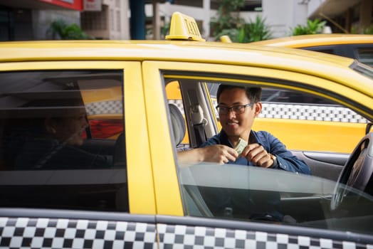 Asian man working as taxi driver in yellow car, with female client paying cash and leaving