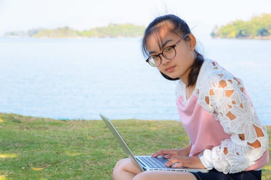 Young girl with laptop on the grass by the lake in park