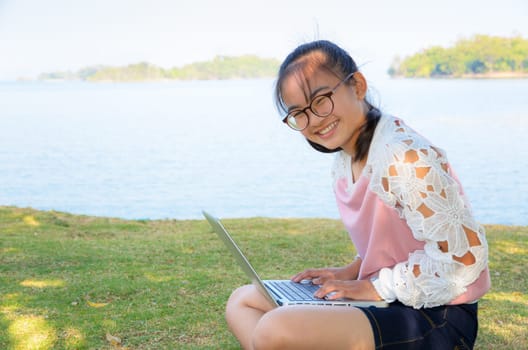 Young girl with laptop on the grass by the lake in park